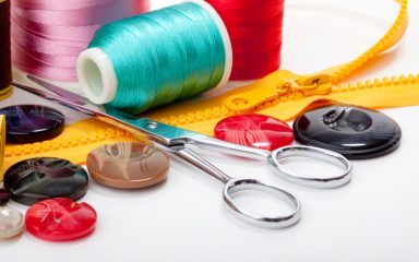 Sewing supplies including thread, button, tape measure, and pins over white background, selective focus